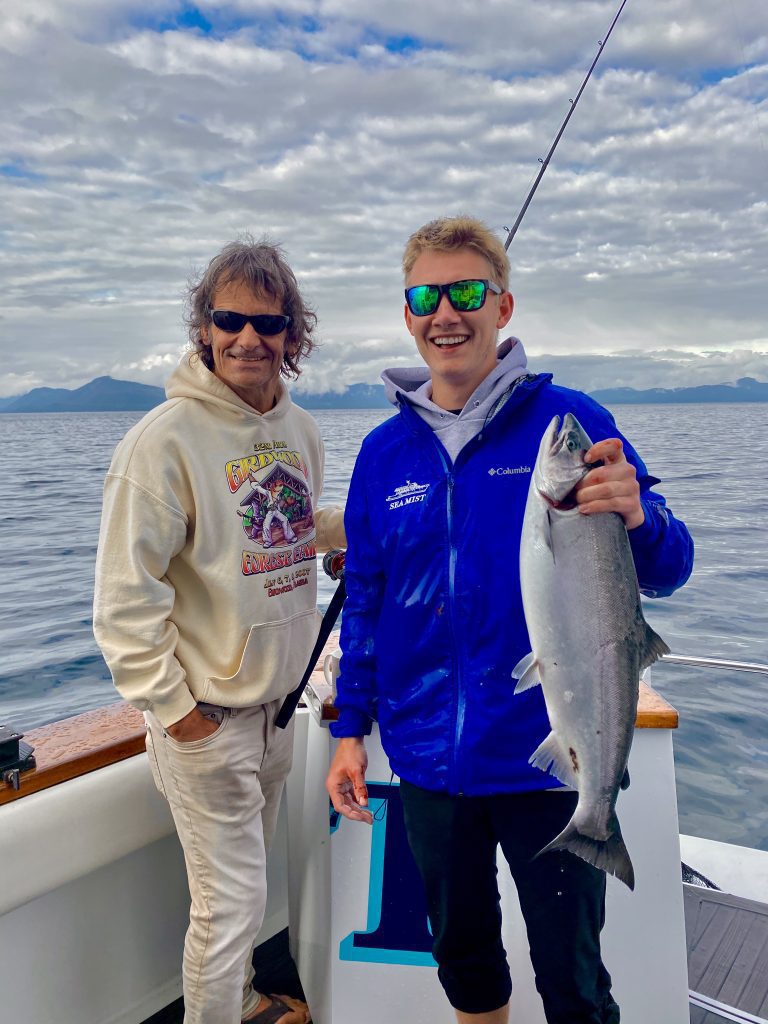 two men holding up a fishing rod and fresh caught Alaskan salmon